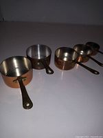 Four vintage copper measuring cups nested on a flat surface, showing varying sizes and brass handles.