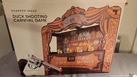Front view of the Sharper Image Duck Shooting Carnival Game with box and toy revolver visible.