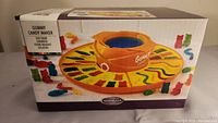 Box front showing the orange circular gummy candy maker and shaped gummy candies on the mold tray.