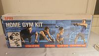Front view of SPRI Home Gym Kit box showing included items: 2 push-up bars, 1 ab wheel, 1 jump rope, and 1 resistance tube along with fitness images.