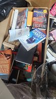 Photo showing a box filled with a large number of paperback books including titles by Marcus Sakey and Lincoln Child