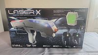 Box front of Laser X gaming set showing one blaster with features highlighted including double blasters, plug in headphones, and 24+ hours playtime.