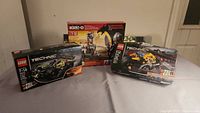 Three boxed sets on a table: two LEGO Technic car models and one KRE-O Dungeons & Dragons set, all new with some box damage