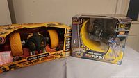 Photo showing two boxed radio control toys: New Bright TumbleBee with yellow wheels, and Monster Jam 360 Flip Set with remote.