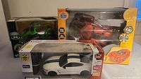 Lot photo showing three radio control cars in box: red Black Widow Racer, white Ford Shelby GT350, green stunt vehicle. Boxes damaged and dirty