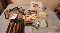 Photo showing entire whittling set including tools, wood block, glove, booklet, sanding block, and carrying pouch spread out on a bed.