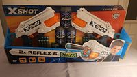Front of box showing dual X-Shot Reflex 6 dart blasters, foam darts, and targets