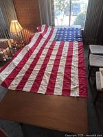 Full view of the 48-star American flag spread out on furniture in a room with a lamp and window behind it.