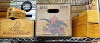 Overall view of multiple wooden boxes and crates: Budweiser 100 year anniversary crate with 1876-1976 markings, wooden wine crates, and other boxes with logos