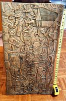 Full view of the wooden carved wall art showing entire depiction and measuring tape alongside for scale.
