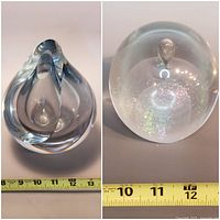 Two piece glass art decor including teardrop sculpture with measuring tape showing 7.5 inches height and spherical glass paperweight with internal bubbles and brass feet showing 4 inches height.