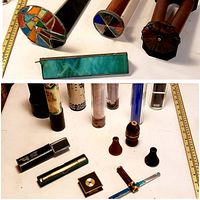 Photo featuring individual kaleidoscopes with cylindrical wooden bodies and colorful glass or paper ends, laid out alongside a measuring tape for length reference.