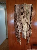 Full view of woven wall hanging artwork displayed on a wooden door showing shape, size, and color schemes.