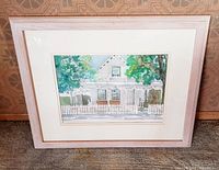 Framed watercolor painting of a white house with picket fence and trees, wood whitewashed frame.