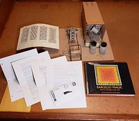 Photo showing a bead weaving loom with beads, two small bead containers, sheets of typed instructions and letters, and a book 'Bargello Magic'.
