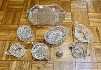 Complete lot of 8 cut glass serving pieces displayed on parquet floor showing variety of shapes and uses.