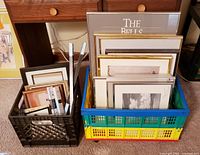 Two crates containing assorted picture frames of varying sizes, styles, and colors including gold, silver, and wood. Frames include glass and matting.