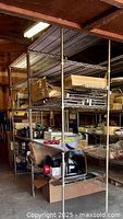Two complete metal wire shelving units with multiple shelves stacked with miscellaneous items, showing overall structure and condition in a warehouse setting.