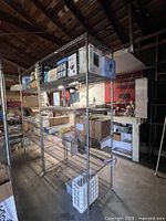 Two tall metal wire shelving units placed in garage or storage space. One is holding various boxes and items, other visible in background. Shows condition and general size/structure.