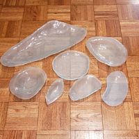Seven translucent Annie Glass pieces arranged on wood floor showing various sizes and organic shapes.