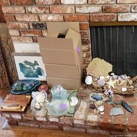 Overview of assorted items on brick hearth including natural shells, coral, wood carvings, glass dishes and fossil specimens with boxes