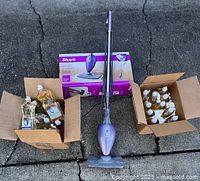 Shark Steam Mop displayed with original box, flanked by two open cardboard boxes containing multiple bottles of dish soap and fly swatters.