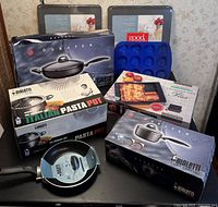 Full set of cookware and bakeware including boxed Bialetti items, Good Cook baking sheets, silicone cupcake pan, and Chef's Design lasagna pan.