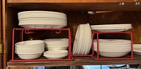 White Corelle plates and bowls stacked on a red metal dish rack.