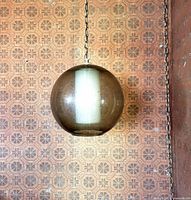 Glass globe hanging light fixture with a metal chain suspended against a patterned wallpaper background, showing the texture and size of the clear glass globe approximately 11 inches in diameter.
