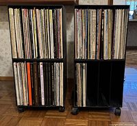 Front view showing two black plastic wheeled vinyl album carts filled with vinyl records, different styles with compartments and dividers