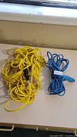 Two coiled extension cords laid on a table, one yellow and one blue, photographed side by side.