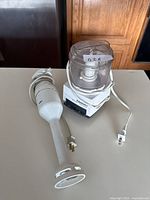 Side view of Braun handheld mixer and Cuisinart food processor placed next to each other on a surface with wooden background.