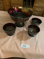 Set of one large and three smaller amethyst carnival glass footed dessert bowls with maple leaf pattern on a peach cloth against a wooden drawer backdrop.