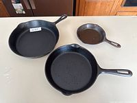 Three cast iron pans displayed on a white surface.