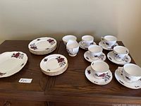 Full set displayed on wooden table showing 6 teacups with saucers, 6 small plates stacked, 6 large plates stacked, cream dispenser, and large serving plate.