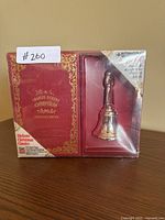 Front view showing red slipcase with gold embossed title and silver plated bell visible in packaging.