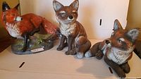 Photo of 3 fox statues showing different poses and colors; one fox shows repair