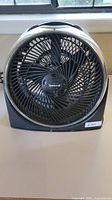 Front view of the Honeywell black box fan on a table, showing the fan grille, blades, and handle on top.