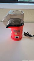 Full front view of red popcorn machine showing plastic top, base, and power cord on white surface.
