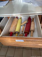 Drawer with five different rolling pins and two small pastry rollers in various styles and colors lying flat.