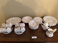 Full view of the entire set laid out on a wooden surface showing plates, bowls, cups, cream and sugar set.