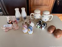 Lot of 11 salt and pepper shaker sets in various shapes, colors, and materials on a white table.