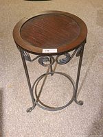 Front view of the round steel frame end table with decorative wooden top showing the scrollwork detail on the frame and circular top surface.