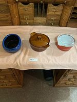 Three vintage glass cookware pieces on cloth - blue bowl, amber casserole with lid, orange Pyrex with lid