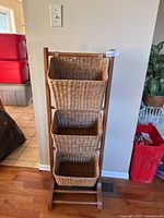 Full view of the wooden rack with three wicker baskets standing against a wall on wood flooring.