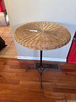 Front perspective of the round wicker tabletop and black metal feet on hardwood floor.