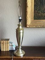 Full view of tall satin old gold colored metal lamp base with an Asian style finial, showing the whole height and shape.