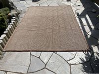 Full view of the 6' x 8' brown carpet laid flat on stone patio, showing overall condition and size.