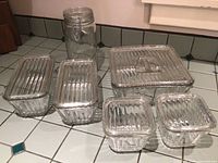 Photo of five ribbed vintage Anchor Hocking glass storage containers with lids, arranged on countertop