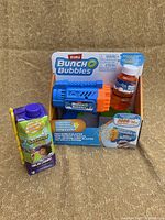 Front view of Zuru Buncho Bubbles Mini Bubble Blaster toy in packaging, alongside Gobbling Bubble Wand bottle.